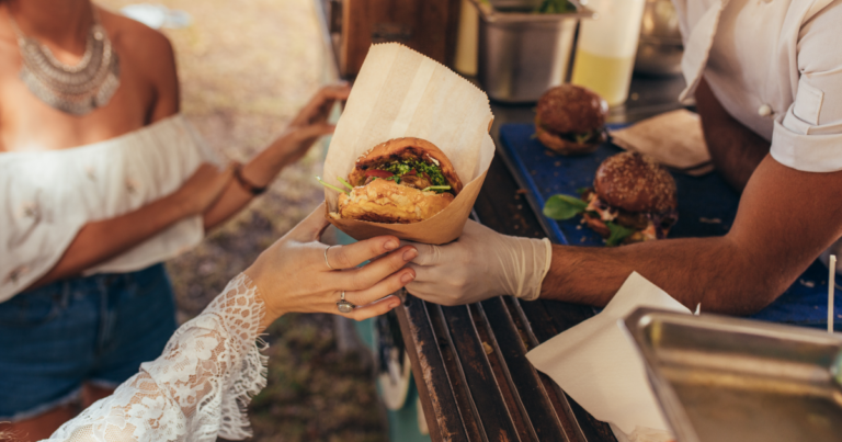 People's hands buying a burger wrapped in paper
